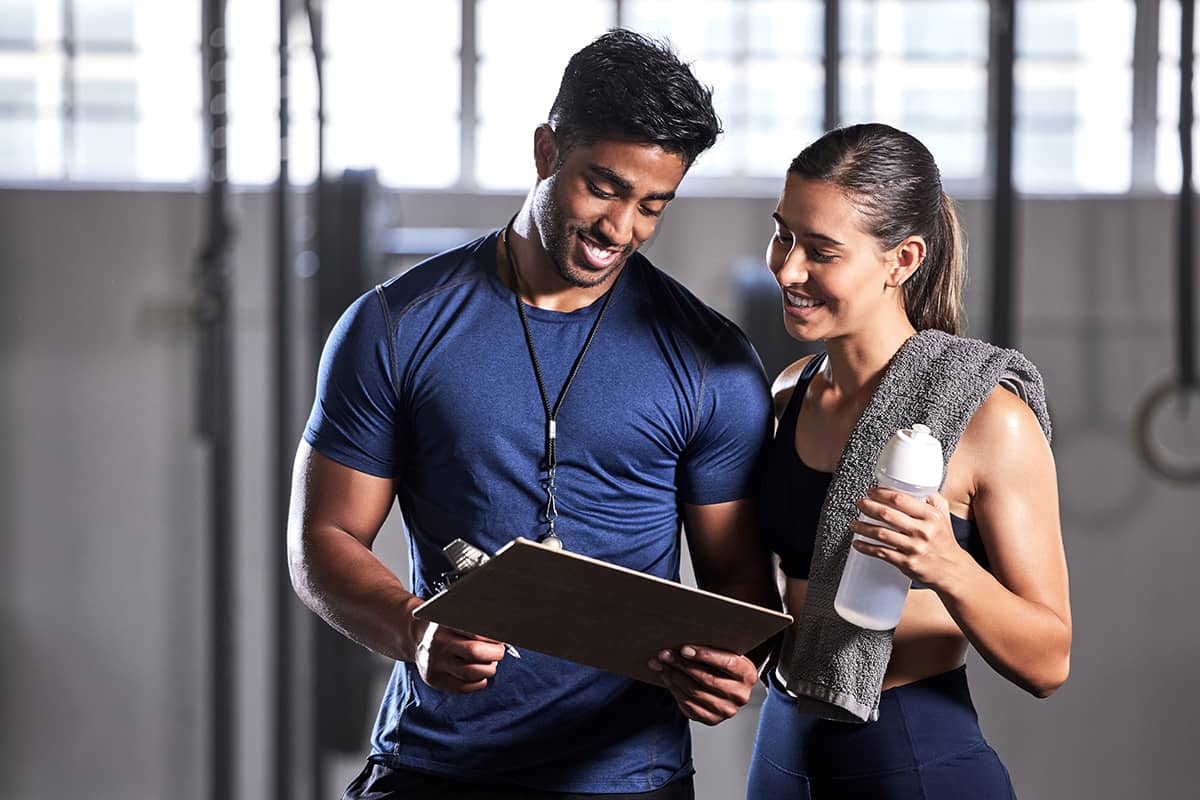 A woman looks over a clipboard with a personal trainer at NJAC in Lawrenceville